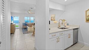 Una cocina moderna con armarios blancos y pomos dorados, un ventanal y vista al océano.