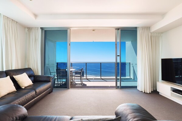 Ein modernes Wohnzimmer mit einer großen Couch, einem Flachbildfernseher und einem Balkon mit Meerblick.