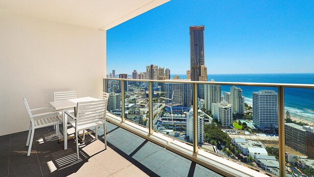 A balcony with a white table and chairs, offering a view of a cityscape and the ocean.