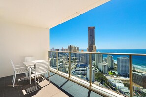 Ein Balkon mit weißem Tisch und Stühlen, der Blick auf eine Stadtlandschaft und das Meer bietet.