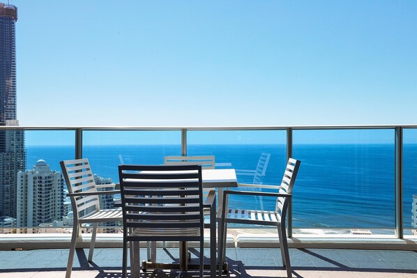 A balcony with two chairs and a table, overlooking a cityscape and the ocean.