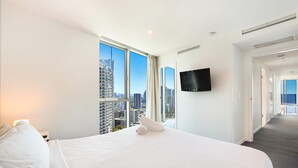A hotel room with a large bed, a flat-screen TV mounted on the wall, and a city view through large windows.