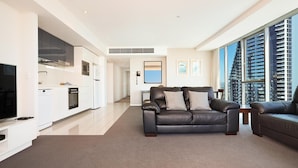 A modern living room with a black leather sofa, a flat-screen TV, and a large window offering a city view.