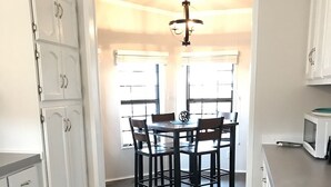 A kitchen with white cabinets, a dining table with chairs, a green rug, and a ceiling light fixture. - The Moon House. Come mingle with the stars. (Hotchkiss)