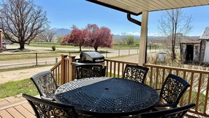A covered patio with a round metal table and chairs, a grill, and a view of mountains and trees. - The Moon House. Come mingle with the stars. (Hotchkiss)