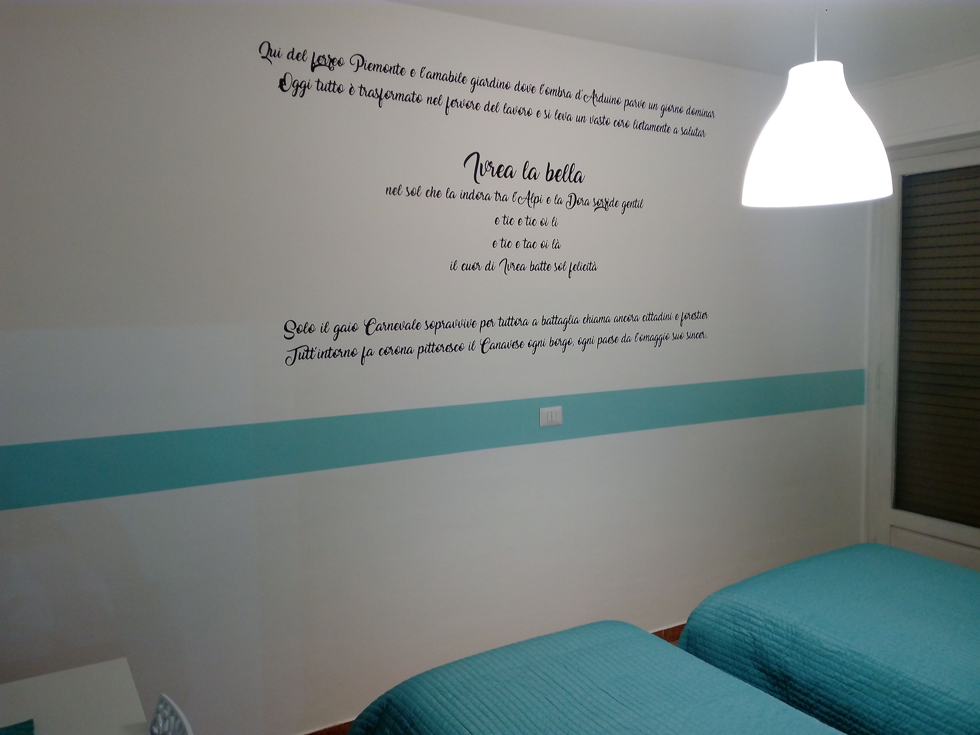 Un dormitorio con una pared de acento color turquesa, dos camas y una lámpara en el techo.