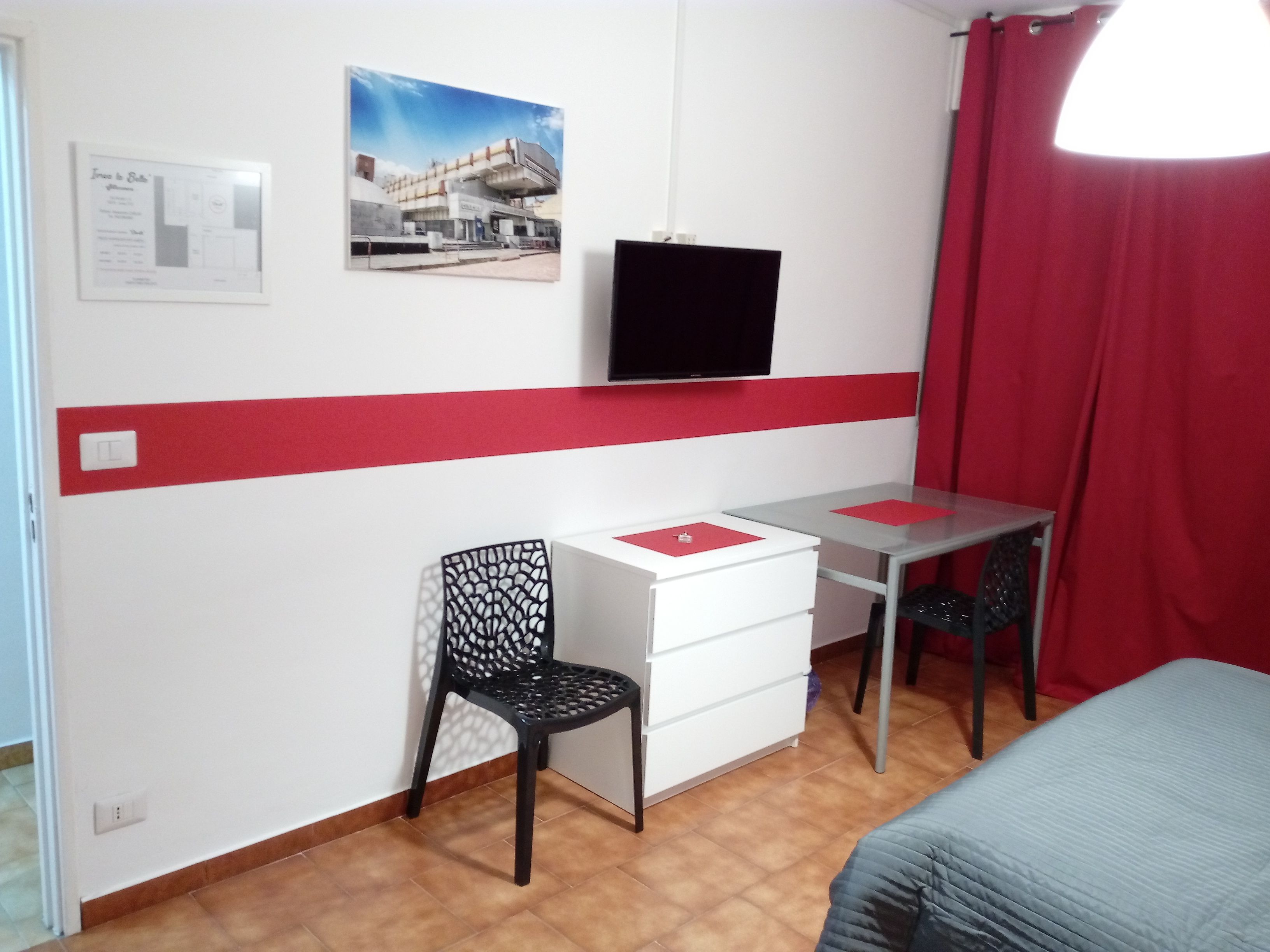 A room with a bed, a desk, a chair, a television, and a red curtain.