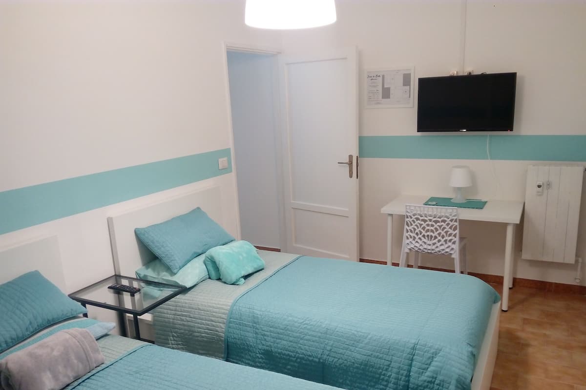 A bedroom with two beds, a desk, a chair, a TV, and a cabinet.