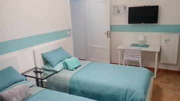 A bedroom with two beds, a desk, a chair, a TV, and a cabinet.