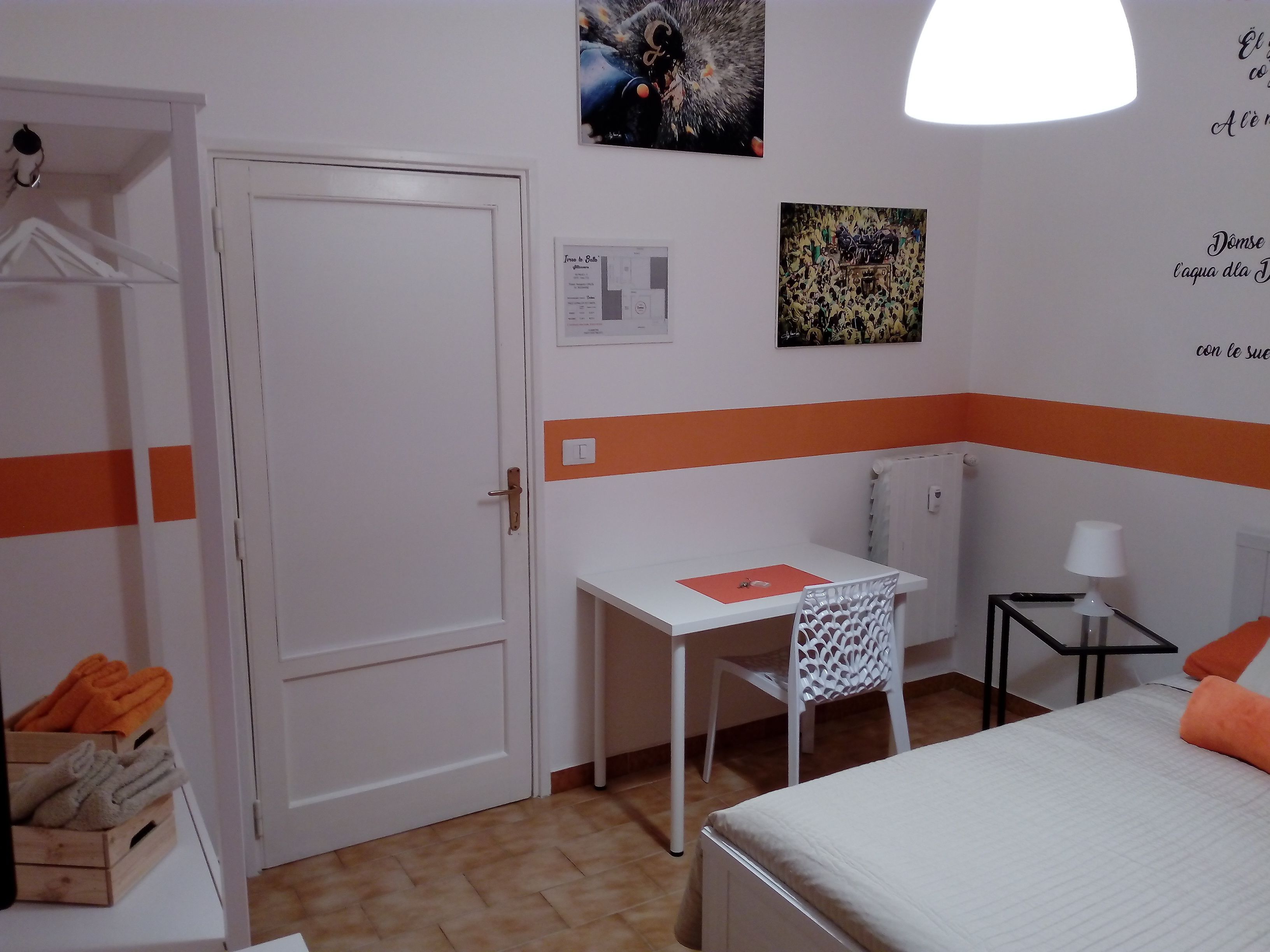 Habitación de hotel con cama, escritorio, silla, mesita con lámpara y armario con toallas.