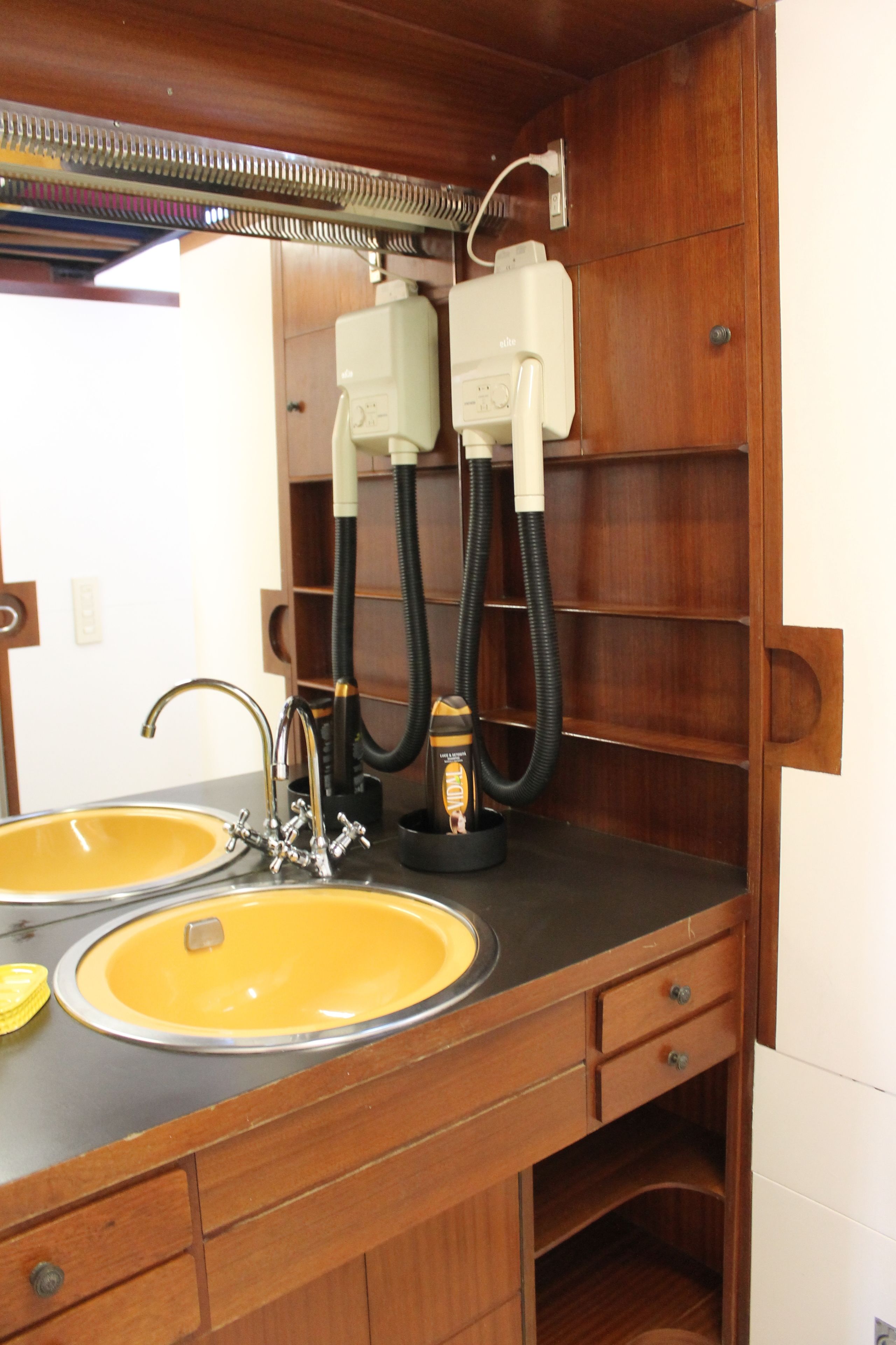 Une coiffeuse en bois avec deux lavabos jaunes, un miroir et un sèche-cheveux.