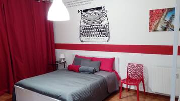 A bedroom with a bed, red curtains, a red chair, a wall with a typewriter illustration, and a radiator.