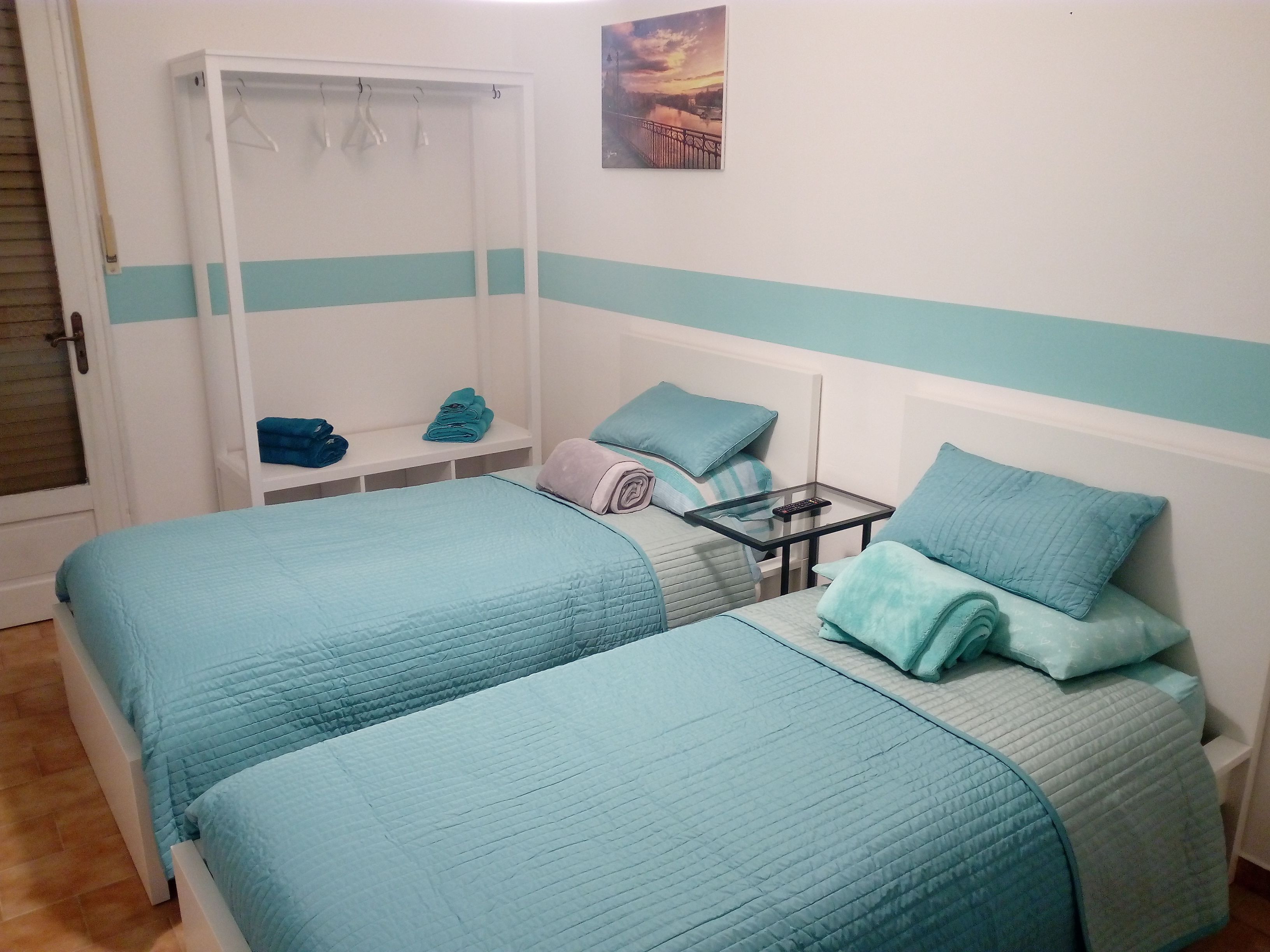 A bedroom with two beds, a wardrobe, and a small table with a remote control.