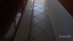 Un couloir étroit au sol carrelé, avec un banc en bois sur le côté gauche et une petite table avec deux chaises au fond.