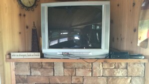 Een televisie op een schoorsteenmantel van natuursteen, een klok aan de muur en een stoel aan de rechterkant.