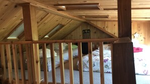 Een slaapkamer op zolder met een houten plafond en houten balustrade. Er staan twee bedden met bloemenbedrukking op.