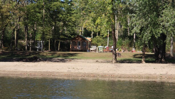 Een vakantiehuis aan het meer met terras, omringd door bomen en een zandstrand.
