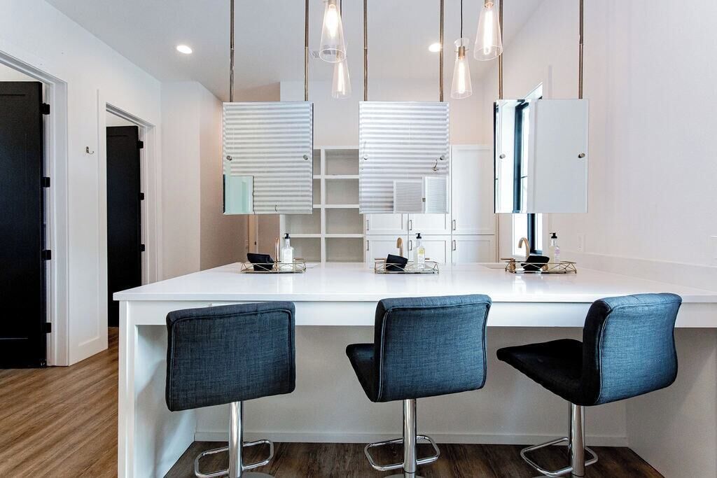 A modern kitchen with a white countertop, three bar stools, and pendant lighting.