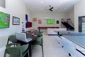 A room with a ping pong table, a desk with a laptop, green chairs, a ceiling fan, and wall-mounted artwork. - Pet Friendly! WalkerVR The Owners House *Texas Oasis* Pool and Hot Tub (Austin)