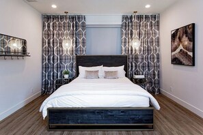A modern bedroom with a large bed, patterned curtains, a bedside table with a lamp, and a framed artwork on the wall. - Pet Friendly! WalkerVR The Owners House *Texas Oasis* Pool and Hot Tub (Austin)