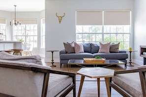 A living room with a sofa, coffee table, and a dining area with a table and chairs. - Pet Friendly! WalkerVR The Owners House *Texas Oasis* Pool and Hot Tub (Austin)