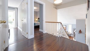 Un hall d’entrée spacieux, doté d’un plancher en bois et de murs blancs, qui mène à une chambre comprenant un lit et une table de chevet.