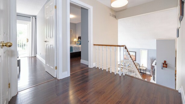 A spacious hallway with wooden flooring and white walls, leading to a bedroom with a bed and a nightstand. - Lake Simcoe Waterfront Retreat | Private Dock, Sandy Beach & Hot Tub (Georgina)