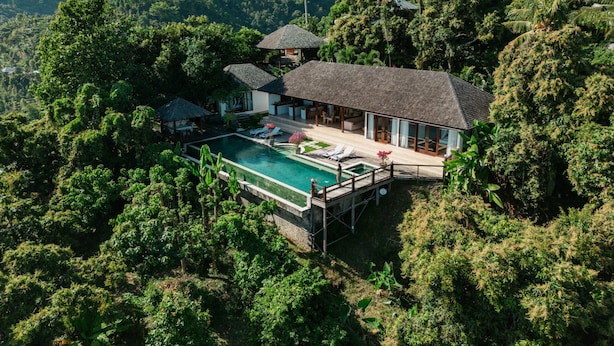 A resort with a swimming pool, a covered patio, and lush greenery surrounding the property.