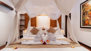 A hotel room with a canopy bed, a painting on the wall, and a bed with towels arranged in a swan shape.