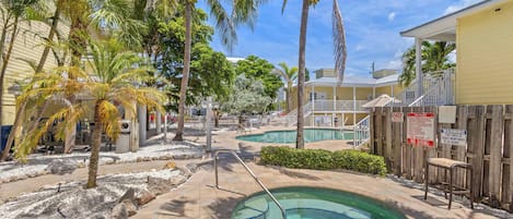 Área de piscina com palmeiras, uma piscina pequena e um cercado de madeira.