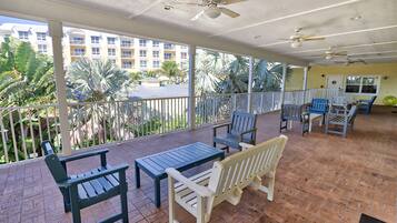 A covered outdoor area with seating, ceiling fans, and a view of a building and palm trees.