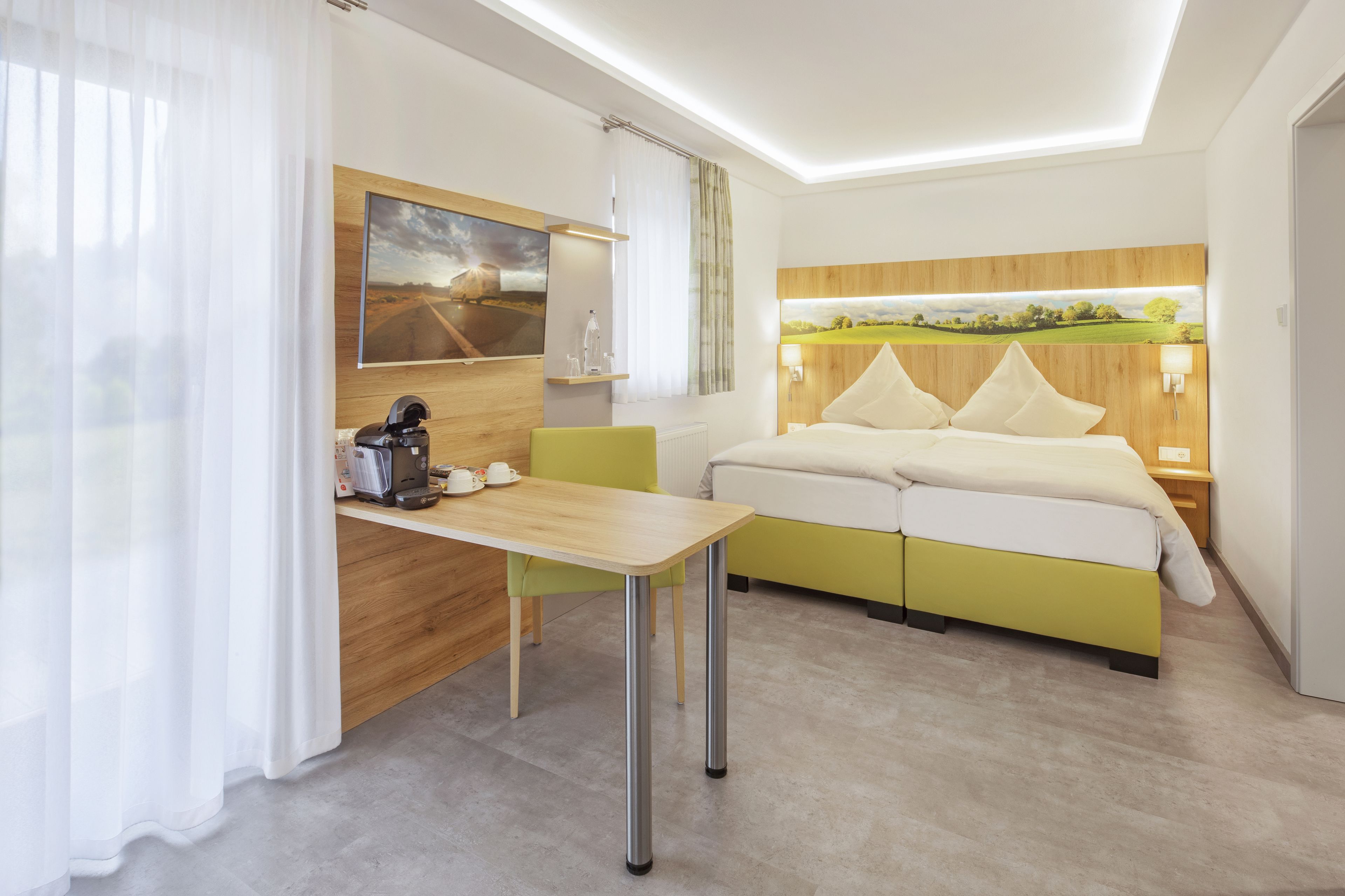 Ein modernes Hotelzimmer mit einem Bett, einem Schreibtisch mit Kaffeemaschine und einem Gemälde an der Wand.