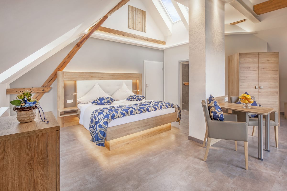 A bedroom with a sloped ceiling, a wooden bed frame, a bedside table, and a desk with chairs.