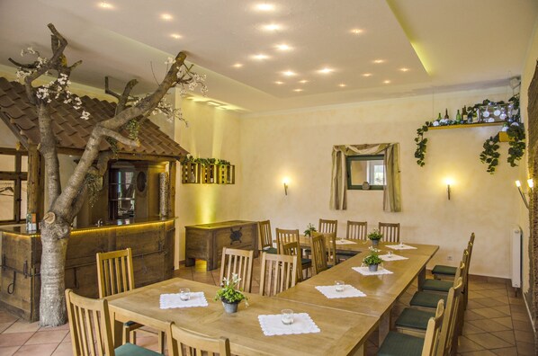 A dining area with a long wooden table, chairs, and potted plants. There is a wooden counter with a mirror and a shelf with bottles. - Brüngers Landhaus (Rödinghausen)