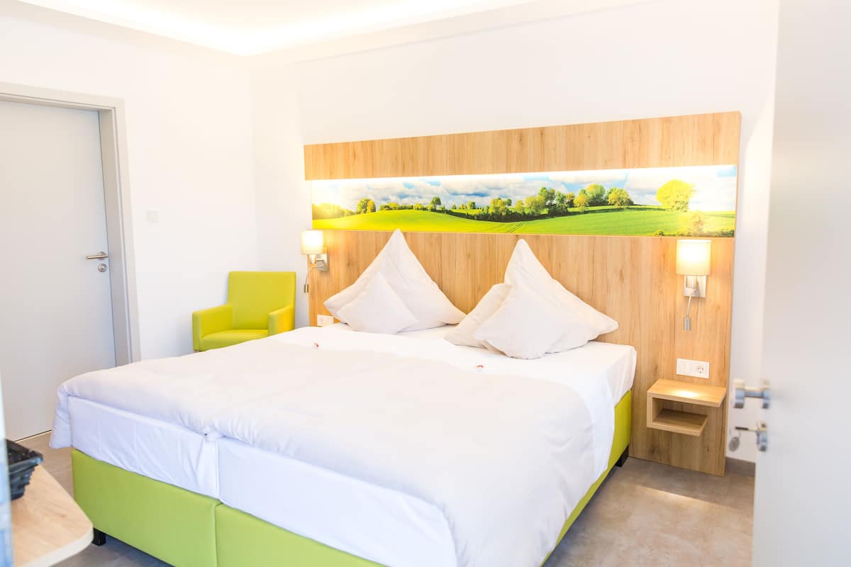 A hotel room with a large bed, a wooden headboard, a painting of a landscape, and a small bedside table.