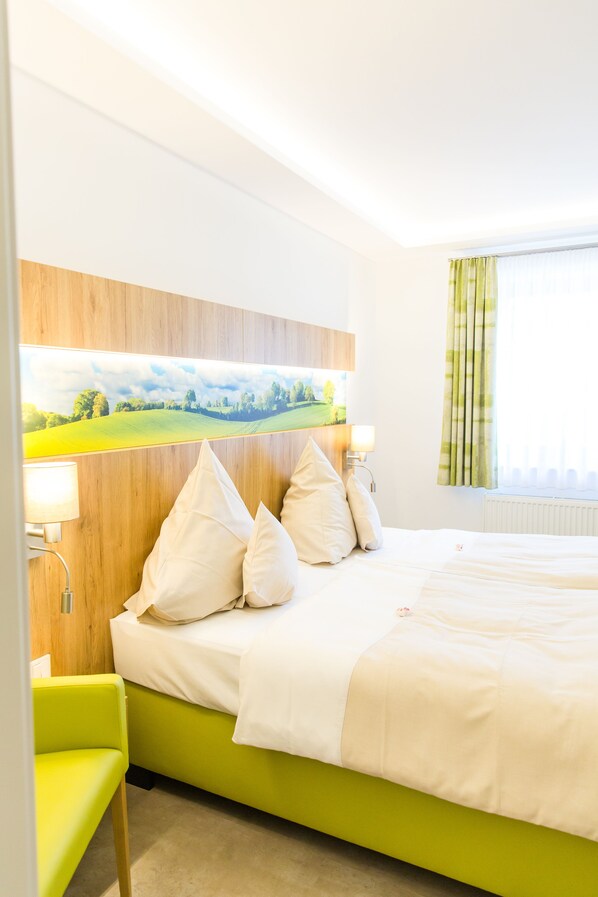 A hotel room with a bed, a green chair, a painting on the wall, and a window with curtains. - Brüngers Landhaus (Rödinghausen)