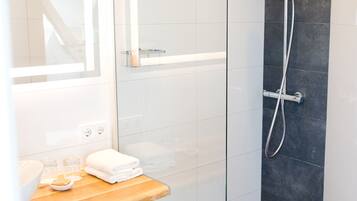 A modern bathroom with a glass shower enclosure, a wooden vanity, and a dark tiled shower wall.