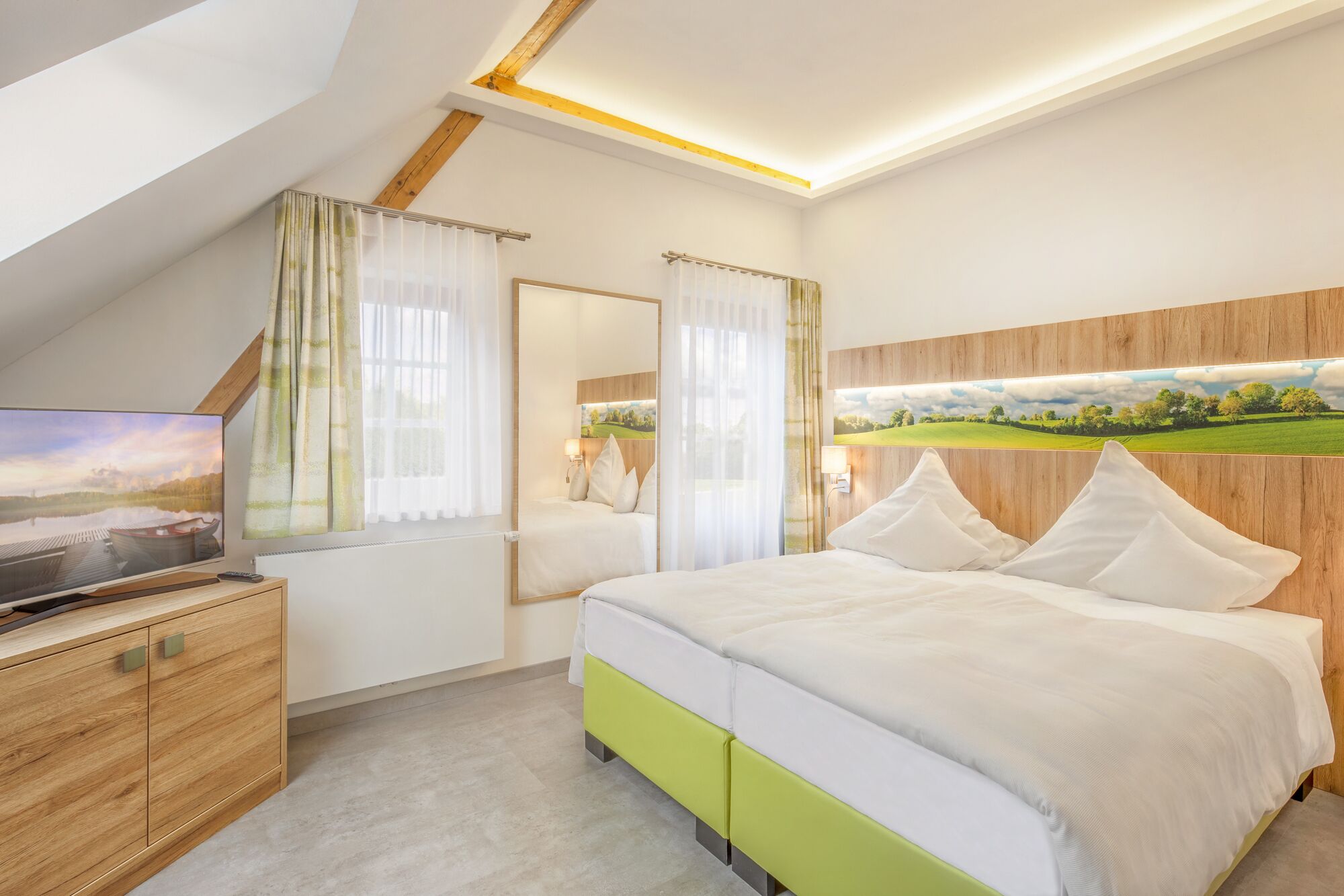 Un dormitorio con una cama, un televisor sobre un mueble de madera, una ventana con cortinas y un cuadro en la pared.