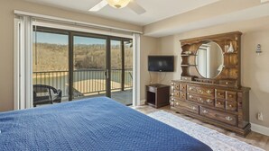 A bedroom with a bed, a dresser, a television, and a balcony with a view.