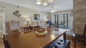 A spacious living room with a dining table, leather sofas, a stone accent wall, and a large window with a view.