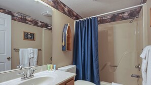 A bathroom with a sink, mirror, toilet, shower, and a blue shower curtain.