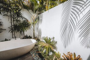 A modern bathroom with a large white bathtub, surrounded by lush tropical plants and a white wall.