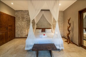 A bedroom with a four-poster bed, a wooden table, and a stone wall.