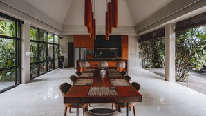 Un moderno comedor con una larga mesa de madera, varias sillas y una cocina al fondo.