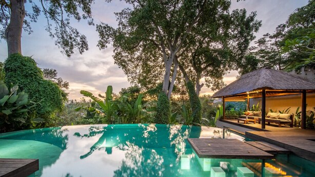A serene outdoor pool area with a wooden deck, a thatched-roof lounge, and lush greenery. - Ubud Villa - 4BR Jungle View (Ubud)