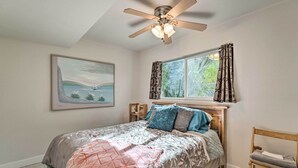 Une chambre à coucher avec un lit, un ventilateur de plafond, une fenêtre avec des rideaux, une chaise et un tableau encadré au mur.