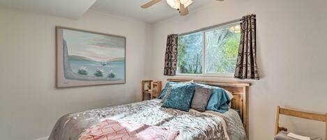 A bedroom with a bed, a ceiling fan, a window with curtains, a chair, and a framed picture on the wall.