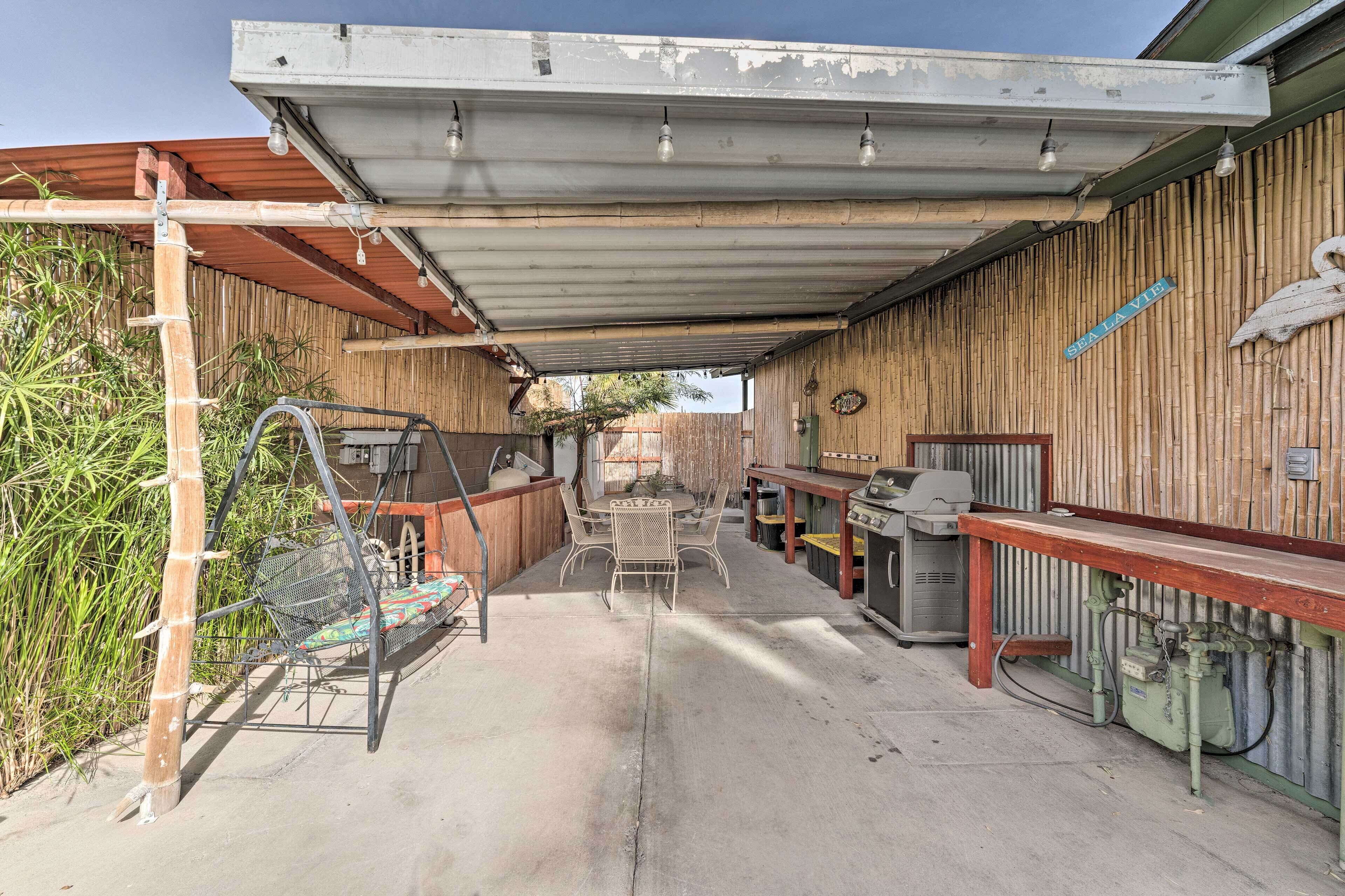 An outdoor patio area with a covered seating area, a grill, and a bamboo wall.