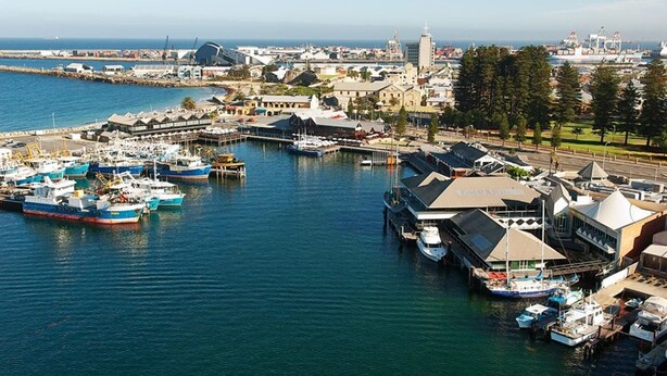 A marina with several boats docked, a prominent building with a dome, and a clear view of the water and distant cityscape. - Great value 2 bedroom apartment in the heart of South Fremantle (Fremantle)