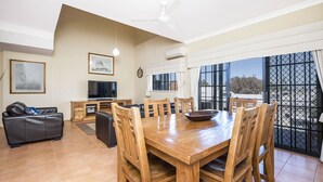 A spacious living area with a wooden dining table, comfortable seating, a flat-screen TV, and a balcony with a view. - Great value 2 bedroom apartment in the heart of South Fremantle (Fremantle)